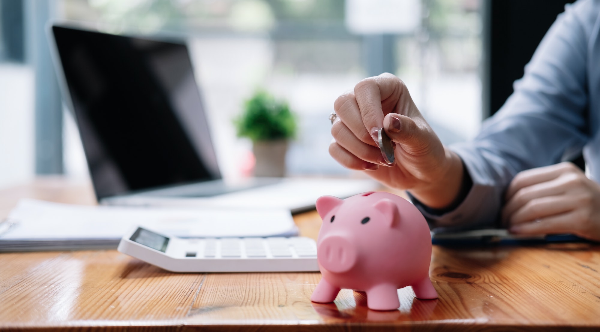 Close up hand of woman putting money coin into pink piggy bank for saving money wealth and
